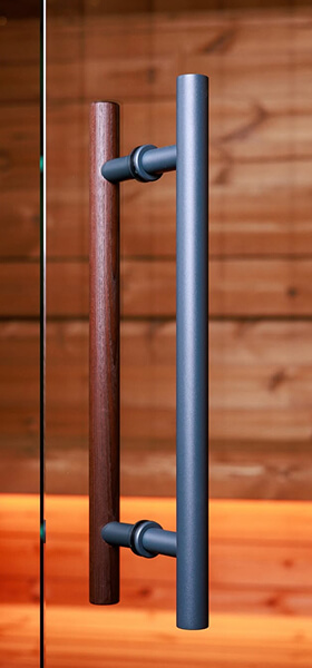 Türgriff mit zwei parallel verlaufenden Stangen, eine aus Holz, die andere aus mattem Metall, vor Holzwand. Türgriff mit zwei parallel verlaufenden Stangen, eine aus Holz, die andere aus mattem Metall, vor Holzwand.