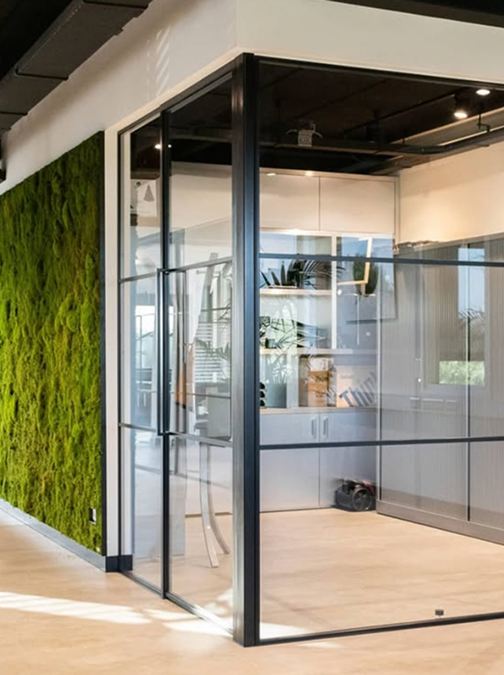 Moderner Büroraum mit Glaswänden, schwarzem Metallrahmen und grüner Mooswand links. Moderner Büroraum mit Glaswänden, schwarzem Metallrahmen und grüner Mooswand links.
